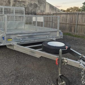 Aluminum utility trailer with a mesh cargo cage on a gravel lot, spare tire mounted on the hitch.