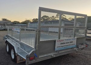 Silver two‑axle utility trailer with mesh sides and a rear ramp, bearing a Logan Trailer Hire banner and phone number on the side plate.