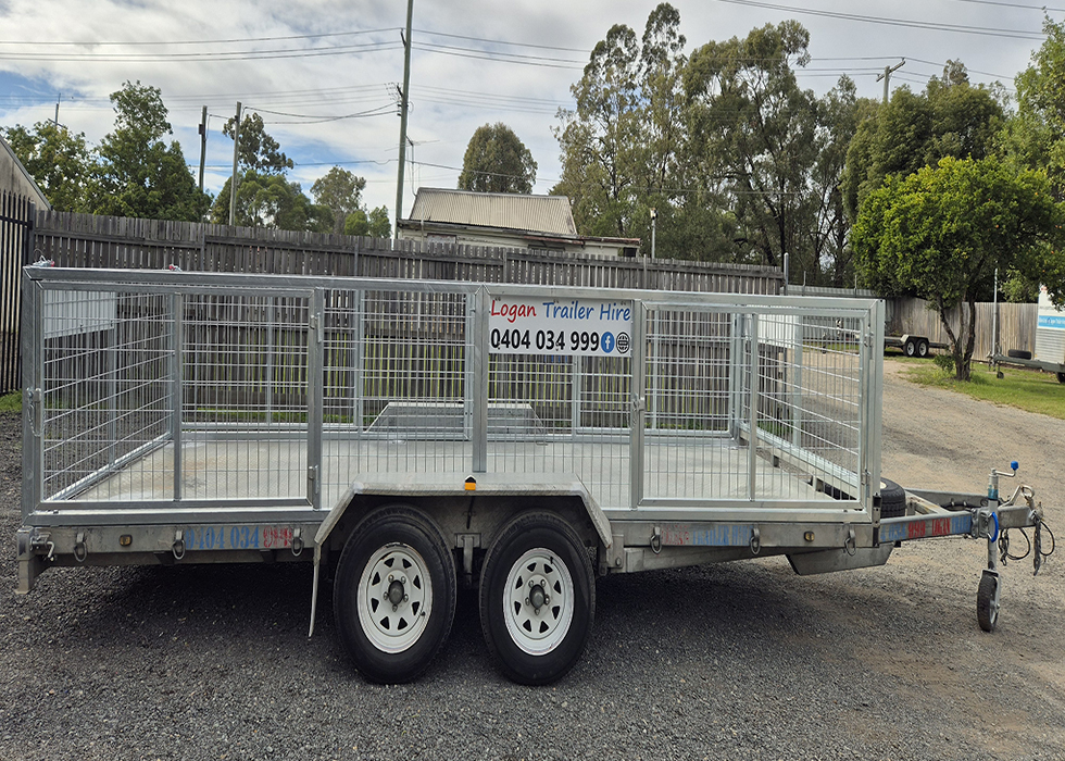 Metal dual-axle utility trailer with high wire mesh sides, advertised for hire with 'Logan Trailer Hire' and phone number 0404 034 999 on the side fence panel.